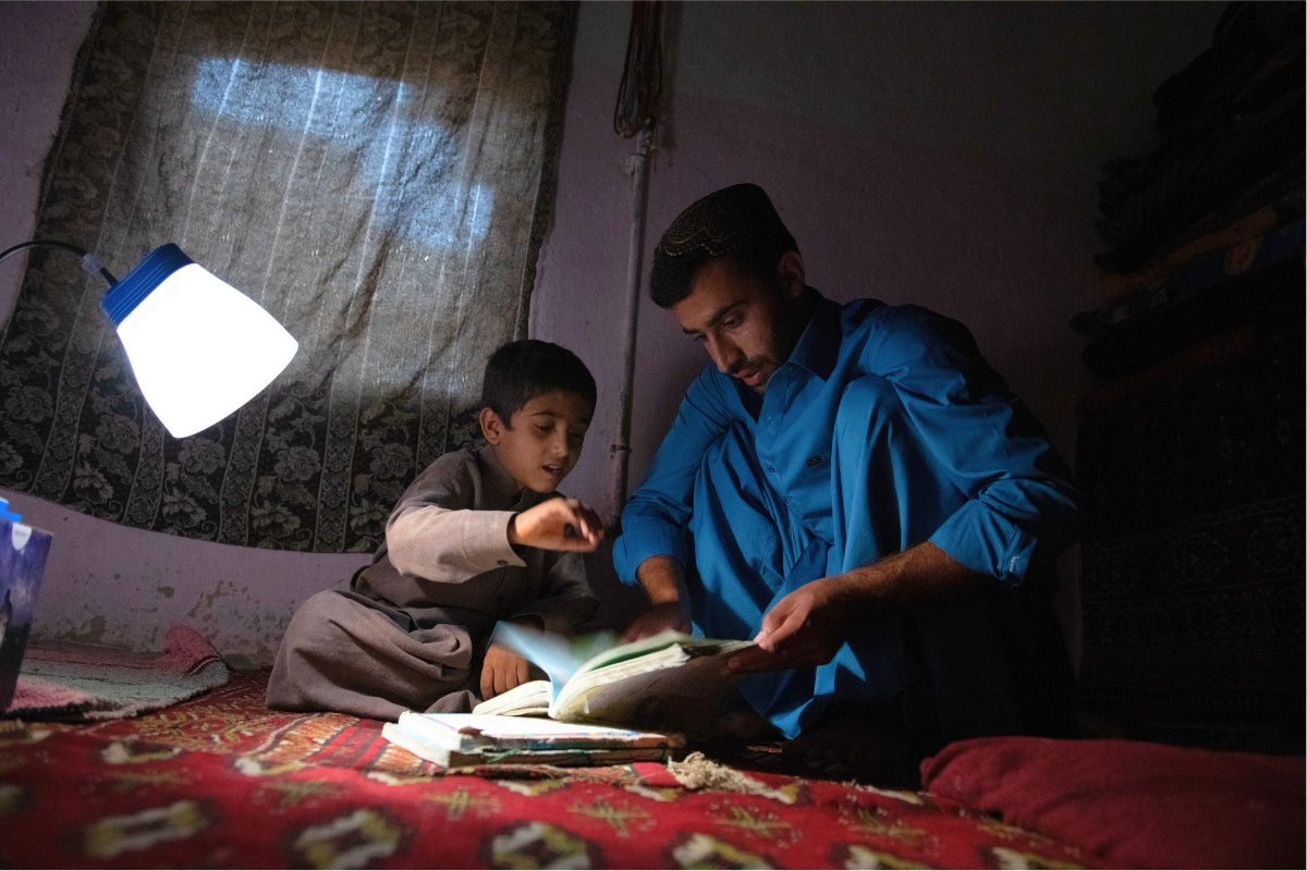 A father helps a son learn in with UNHCR solar lamp