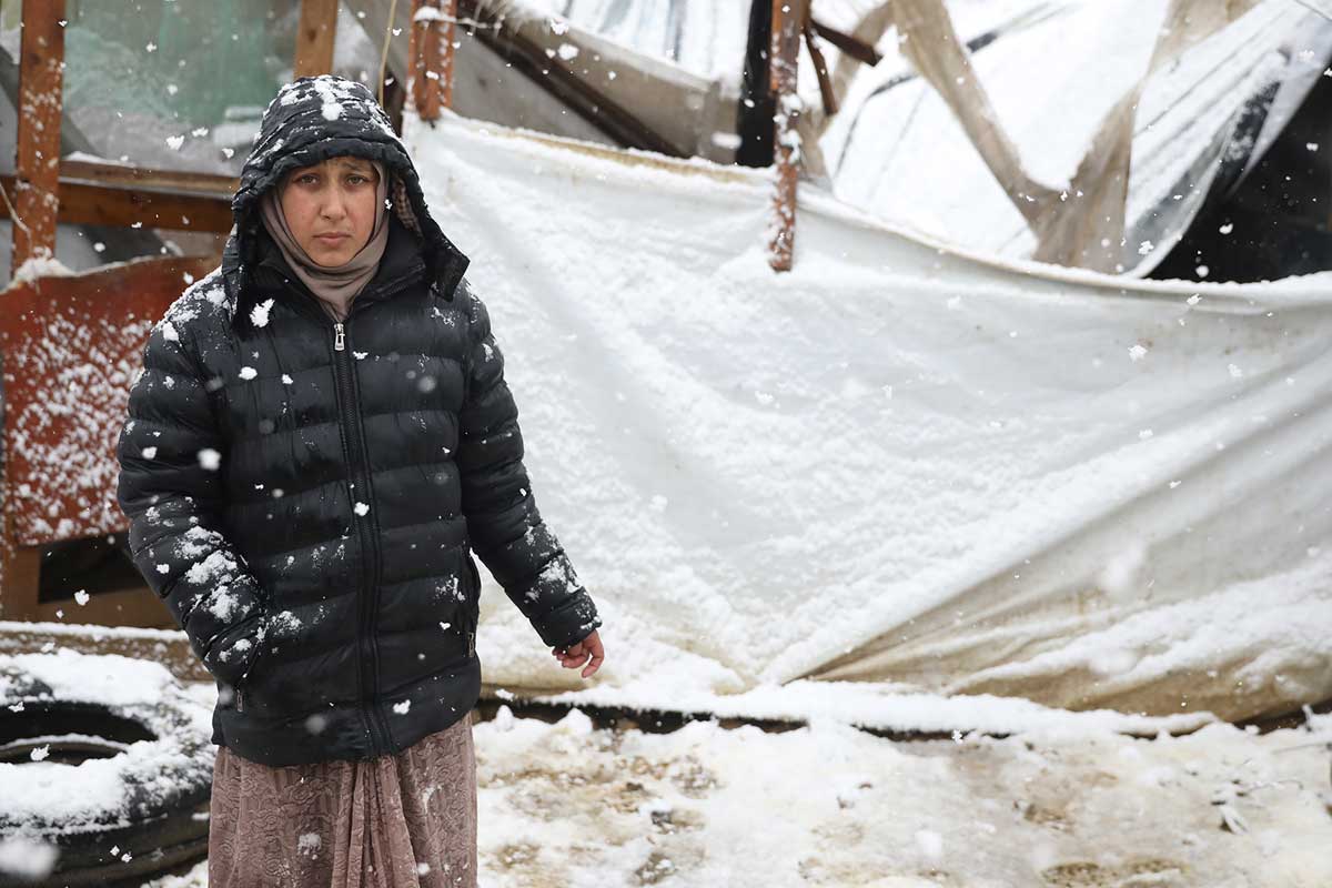 A refugee stands in front of a collapsed building